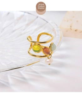 Detail view of gold layered ring with multi-color gemstones and a pearl drop charm