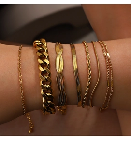 Detailed view of stacked 18K gold plated Cuban and flat snake chains on a female wrist