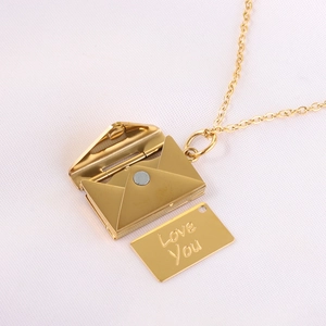 Detail of gold envelope pendant necklace with 'Love You' engraved card on white fabric