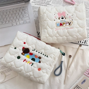 Detail of heart-quilted puppy makeup bag with embroidery and laptop on a desk