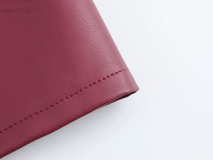 Detailopname van wijnrood PU-leer met fijne textuur en nette stiksels op de stof