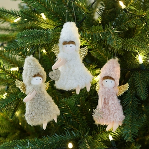 Three plush Christmas angel dolls in white, beige, and pink hanging on a warm lit Xmas tree
