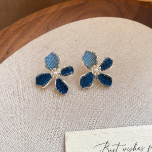 Close-up of denim flower earrings with silver edges and white pearl centers on fabric