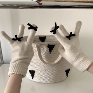 Close-up of cream knit gloves with black bow details on fingers and ribbed cuffs