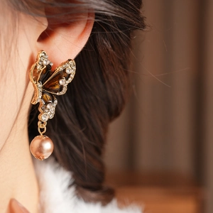 Close-up of vintage butterfly earring with brown enamel and pearls on a model