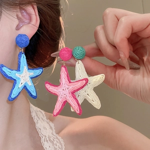 Detail view of woven raffia starfish earrings in blue, pink, and cream white colors