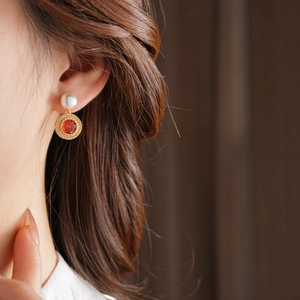 Détail d'une boucle d'oreille dorée avec perle et zircon rouge sur un mannequin