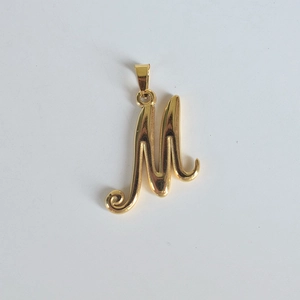 Détail macro du pendentif monogramme lettre M en acier inoxydable plaqué or 18 carats poli