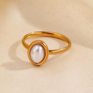 Fashionable gold oval ring featuring a white faux pearl inlay on warm beige fabric background