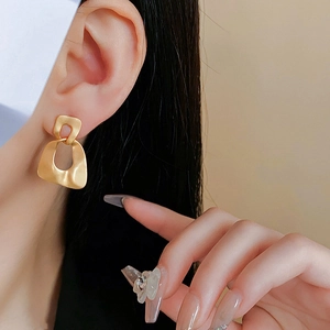 Close-up of matte gold geometric earring showing frosted texture on human ear
