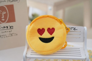 Detail of yellow plush emoji coin purse with heart-eyes embroidery on a white bench