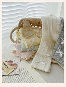Close-up of pastel knitted socks with delicate white bow accents in a woven basket