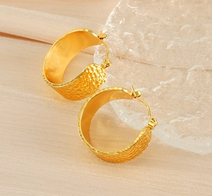 Détail macro de boucles d'oreilles dorées martelées en C sur plateau en verre