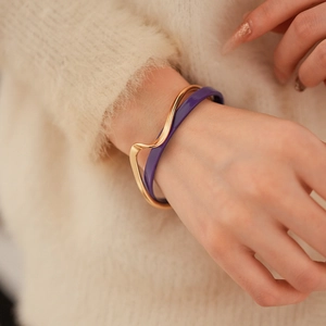 Detail of a purple enamel ring bracelet and a wavy gold bangle worn on a sweater