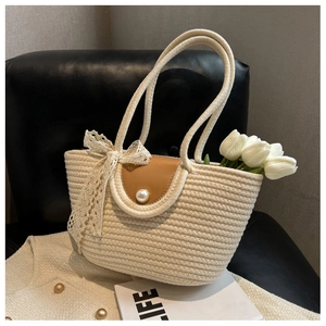Detail of straw woven tote bag featuring brown leather flap and large pearl button accent