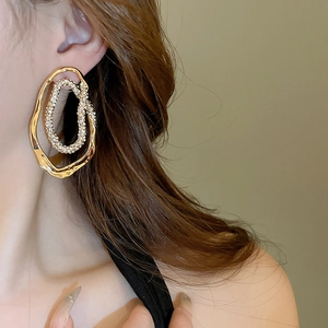 Detail showing gold irregular oval hoop earrings with sparkling diamonds on a model