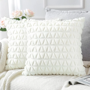 Close-up of white plush pillow covers with 3D geometric patterns on a soft sofa