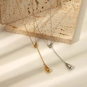 Artistic detail of gold and silver teardrop lariat necklaces on a stone with soft shadows