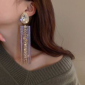 Close-up of golden long tassel earrings with royal blue and clear waterdrop rhinestones