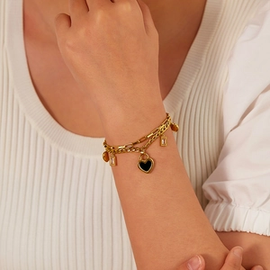 Detail of a gold double-layer bracelet with black heart and rectangular crystal charms