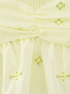 Détail du tissu jaune clair avec broderie fleurie verte et texture plissée sur le haut