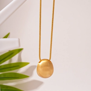 Close-up of a matte gold oval pebble pendant on a delicate snake chain necklace