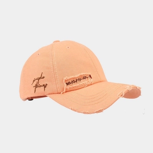 Close-up of orange cotton baseball cap featuring distressed holes and side embroidery
