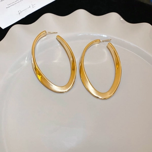 Detail view of gold chunky twisted oval hoop earrings resting on a white ceramic plate