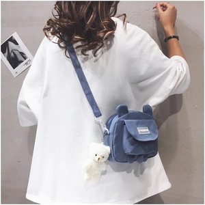 Detail of blue canvas bear crossbody bag with white plush charm and adjustable strap