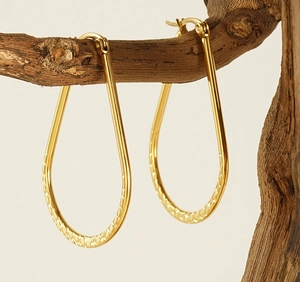 Détail de boucles d'oreilles goutte dorées avec texture martelée sur branche bois