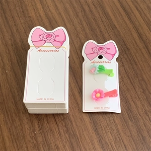 Detail view of pink and green floral hair clips displayed on white bow-tie themed cards