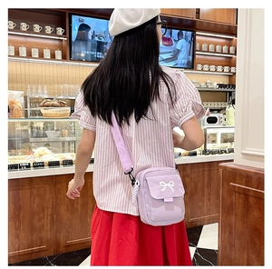 Detail of purple crossbody bag with white bow and adjustable strap on a model