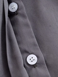 Close-up of charcoal grey fabric texture with white four-hole buttons on shirt