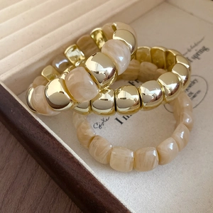 Close-up of golden metal and marble resin beads layered in a velvet jewelry box