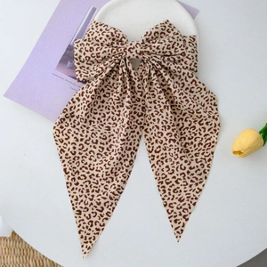 Detailed view of large leopard print bow hair clip with long ribbons on white plate