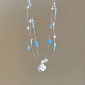 Summer ocean layer necklace with blue beads and silver scallop pendant on khaki background
