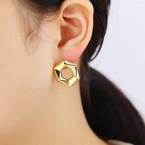 Macro side view of a model wearing high-polish golden hexagonal geometric metal earrings