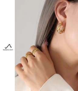 Detail of gold-plated twisted U-shape earrings and stackable rings set on model
