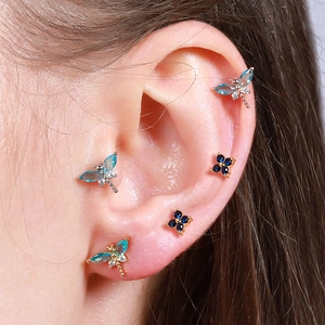 Detail shot of dragonfly and flower piercing studs with blue zircons on the ear