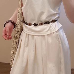 Detail showing handcrafted wooden bead waist chain and chunky resin bangle on white dress