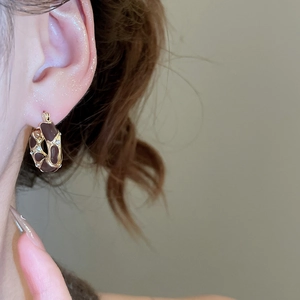 Close-up of golden hoop earring with brown enamel and crystals worn by a model