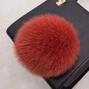 Vue détaillée d'un pompon en fourrure de renard orange sur un sac en cuir texturé noir