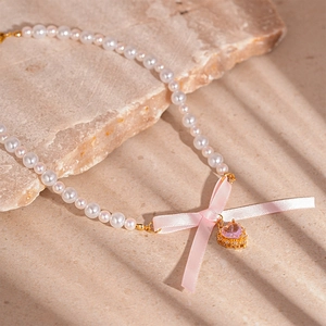 Close-up of pearl necklace featuring a pink silk bow and sparkling heart pendant on a stone