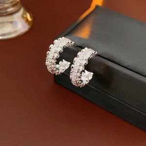 Macro detail of silver C-shaped earrings with wave edges and sparkling cubic zirconia stones
