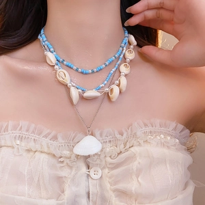 Detail of 4-piece layered ocean necklace with beads and shell charms on a white lace top