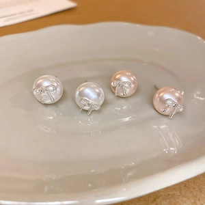 Elegant bow knot faux pearl earrings in white and pink displayed on a ceramic tray
