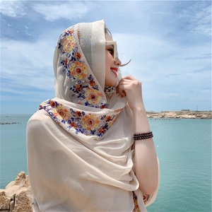 Close-up of a beige summer shawl featuring colorful floral embroidery on a scenic beach