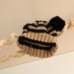 Berretto in maglia a righe per bambini con due pompon su un supporto di legno