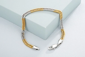 Detail of two-tone gold and silver Cuban link bracelet with lobster clasp on blue block