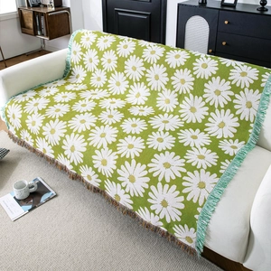 Floral jacquard knit blanket with green daisy patterns and colorful tassel edges on a sofa